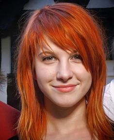 a woman with red hair and bangs smiling at the camera while two other people stand behind her