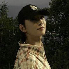 a man wearing a baseball cap standing in front of some trees and water at night