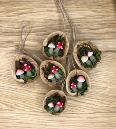 four small mushrooms are placed in wooden bowls with moss and stones inside them on a table