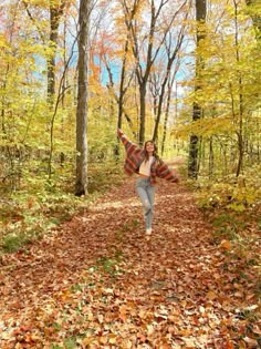 a woman walking down a leaf covered path in the woods with her arms spread out