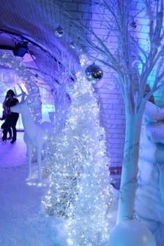 two white deer statues next to a tree with blue lights and snow on the ground