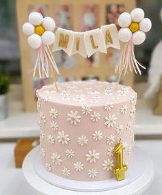 a pink cake with white flowers on top and the name mia spelled in gold letters