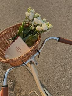 a basket with flowers and a book on the handlebars of a bicycle in the sand