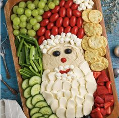 a wooden platter filled with cheese, crackers and veggies in the shape of santa clause