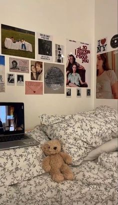 a laptop computer sitting on top of a bed next to a teddy bear and pictures