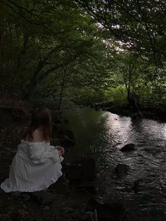 a woman in white dress sitting on rocks next to river