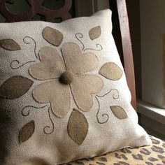 a pillow with a flower on it sitting in front of a window next to a chair