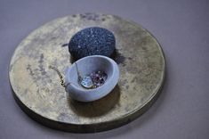 two pieces of jewelry sitting in a small bowl on a gold plate with a chain