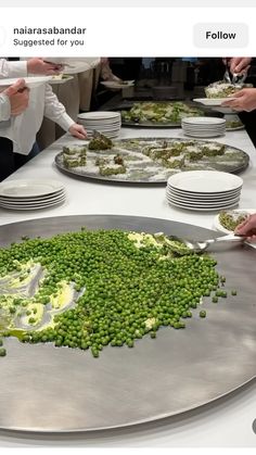 several people standing around a table covered in plates with peas on them and one person holding a plate