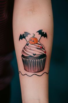 a cupcake tattoo with bats and a pumpkin on the top is shown in color