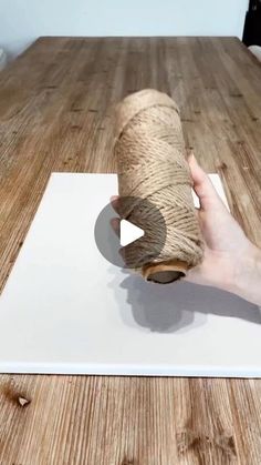 a person holding a roll of twine on top of a wooden table next to a white piece of paper