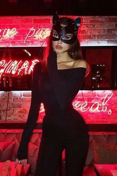 a woman wearing a cat mask standing in front of a neon sign