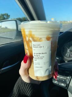 a woman holding up a cup of iced coffee in her hand while driving down the road