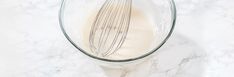 a whisk is in a glass bowl on a marble counter top, next to milk