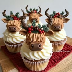 three cupcakes decorated with reindeer heads and holly decorations on top of a wooden table