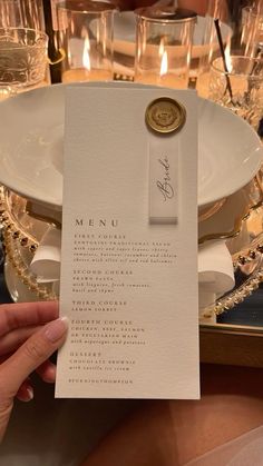 a person is holding up a menu card on a table with candles in the background