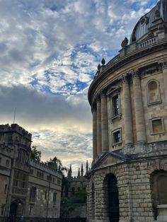 an old stone building with a clock tower in the background and cloudy skies above it