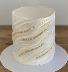 a white cake with gold beads on it sitting on a plate next to a wooden table