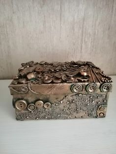 a decorative box with buttons and chains on the lid sitting on a white table top