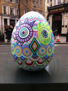 a large colorful egg sitting on top of a black table in front of a building