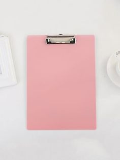 a pink clipboard next to a coffee cup and saucer on a white table