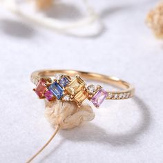 a gold ring with multicolored stones and diamonds on it sitting on a white surface