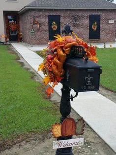 a mailbox decorated with fall leaves and pumpkins in front of a brick house