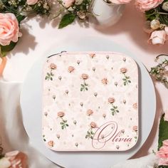 a white plate topped with pink flowers and a personalized coin purse on top of it