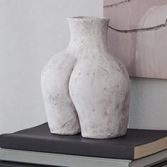 two white vases sitting on top of a book next to each other in front of a painting