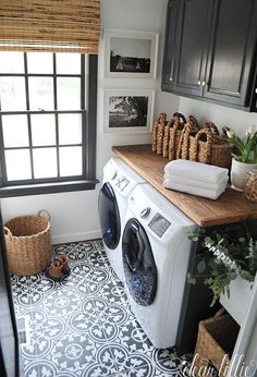 a washer and dryer in a small laundry room with black cabinets, wood counter tops, and patterned floor tiles