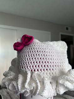 a white crocheted hat with a pink bow on it's head sitting on top of a bed