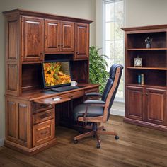 a computer desk with a laptop on it in front of a bookcase and cupboards