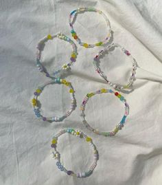 four bracelets with colorful beads are on a white cloth covered tablecloth in the shape of circles