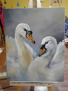 two white swans with their heads touching each other's necks in front of a painting