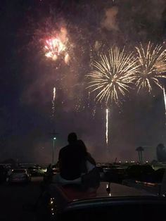 people sitting on the hood of a car watching fireworks go off in the night sky