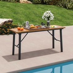 an outdoor table with food on it next to a pool in the grass and flowers