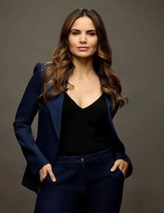 a woman in a black top and blue blazer posing for the camera with her hands on her hips