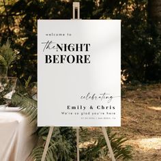 a white sign sitting on top of a wooden easel next to a table covered in greenery