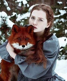 a woman is holding a red fox in the snow with her hands on her chest