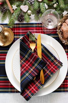 a place setting with plaid napkins, gold forks and pine cones on the table