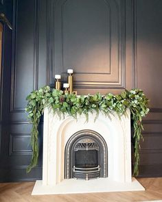 a fireplace with candles and greenery on it in a room that is painted black