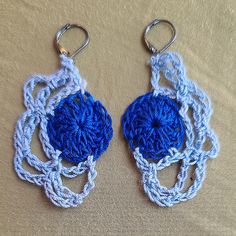 two crocheted blue and white circular objects on a beige surface with metal hooks