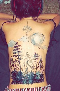 the back of a woman's body with trees and mountains painted on her stomach