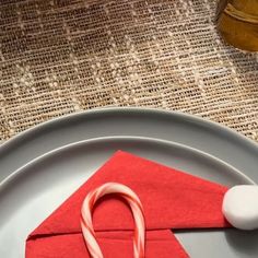 an origami candy cane sits on a plate next to a piece of red paper