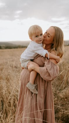 a woman holding a baby in her arms while standing in the middle of a field