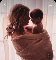 a woman is holding a baby wrapped in a blanket while she looks out the window