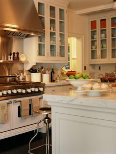 a kitchen with white cabinets and marble counter tops, an island in the middle is surrounded by stainless steel appliances