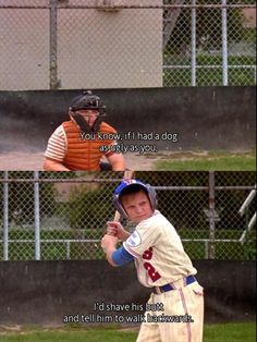 a baseball player holding a bat in front of a fence and another man behind him