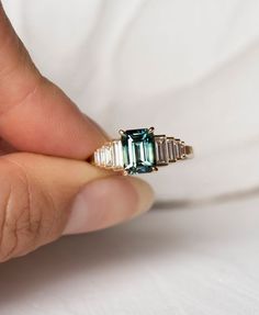 a woman's hand holding an emerald and diamond ring with three baguettes