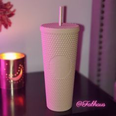 a pink cup sitting on top of a table next to a candle and a vase